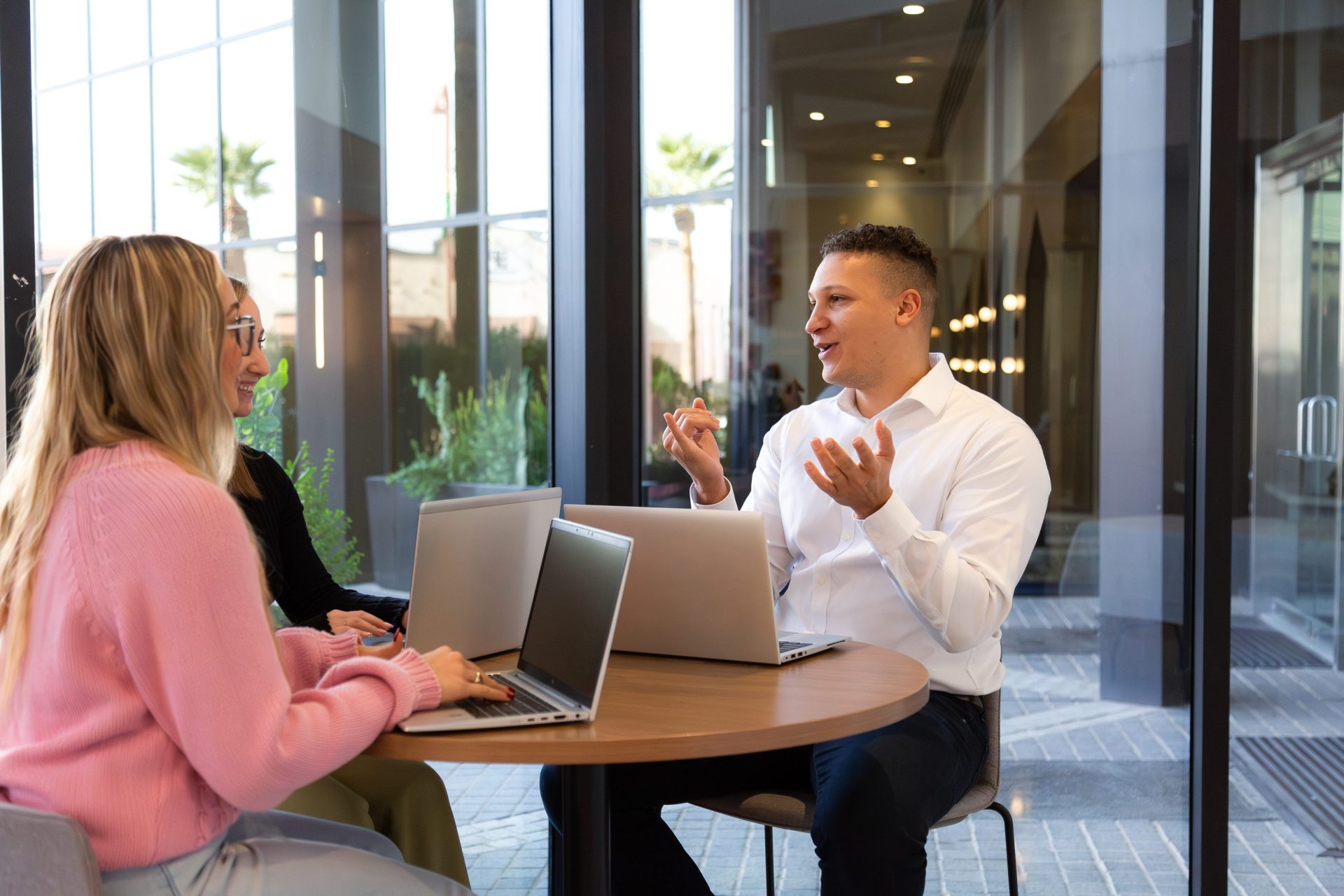 Team members sitting at a co-working table with their laptops while speaking to eachother