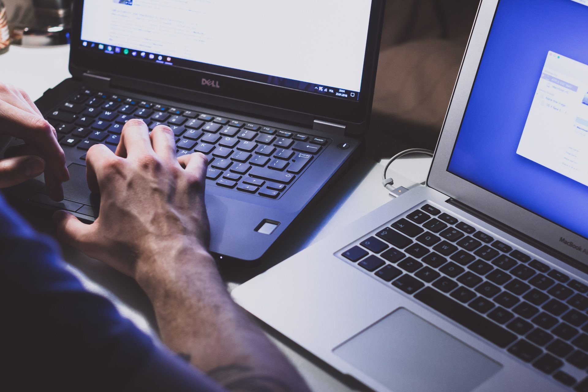 Two laptops open, one Dell and one Apple with a man working on them at the same time.